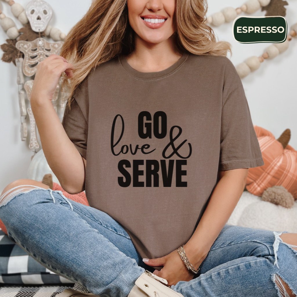 Woman wearing a brown t-shirt with 'GO love & SERVE' text, sitting in a cozy room.