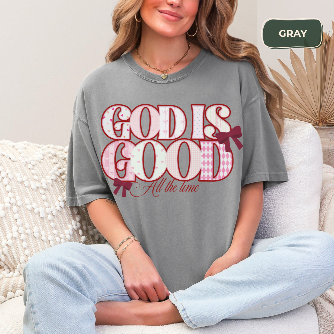 Person wearing a gray t-shirt with 'God is Good All the time' text, sitting on a white couch.