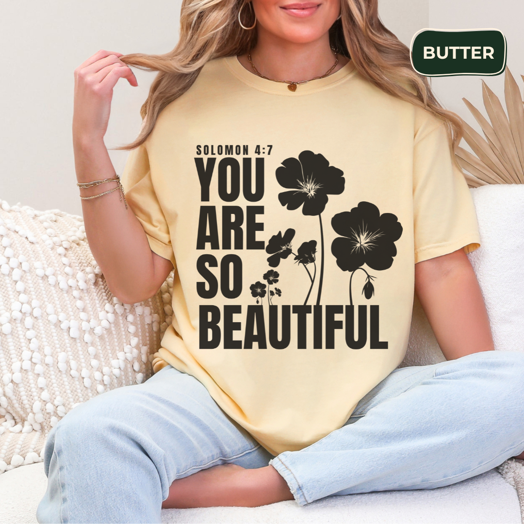 Woman wearing a yellow t-shirt with floral design and text, sitting on a couch.