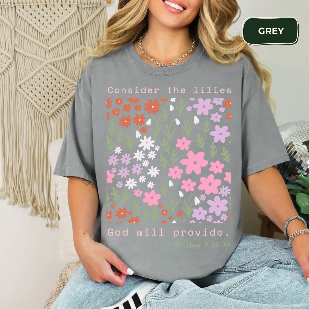 Person wearing a gray t-shirt with floral design and text, sitting against a textured wall.