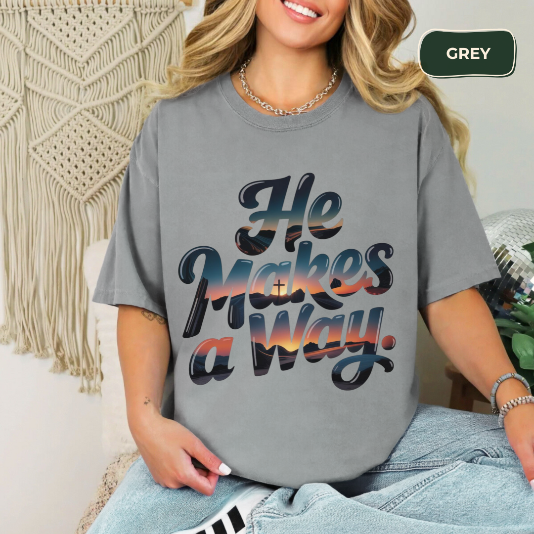 Person wearing a gray t-shirt with colorful text, sitting against a textured wall.