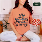 Woman wearing a peach t-shirt with text, sitting in a kitchen holding a mug.